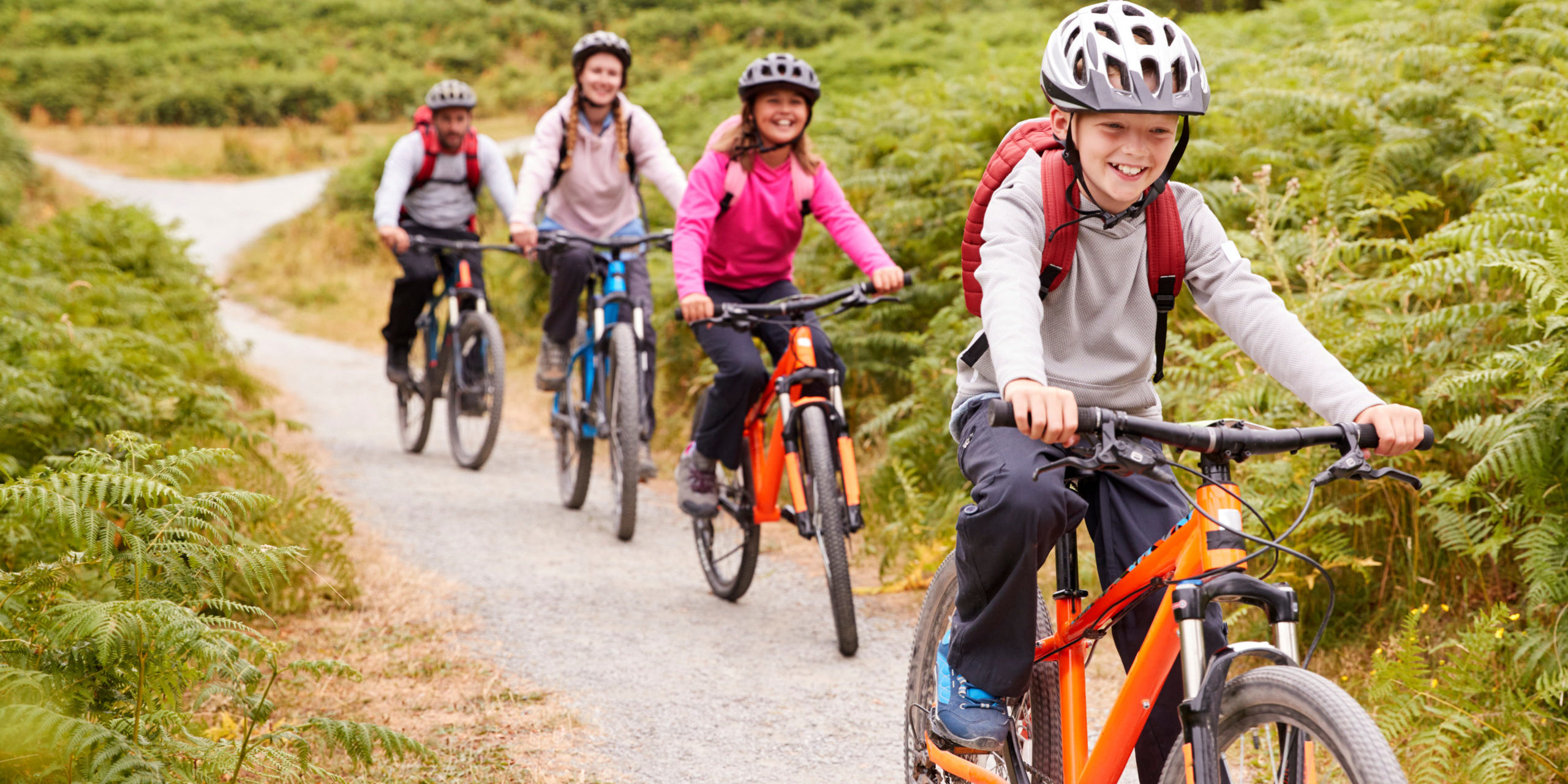 Fahrradwege für Familien: 4 köpfige Familie fährt mit Rädern und Helm durch eine Naturlandschaft